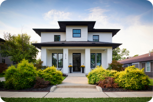 Front view of a modern white two story home with black trim, large covered porch, and well kept landscaping.