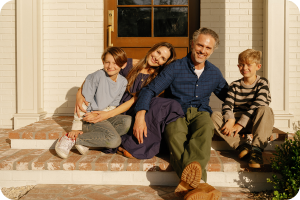 Family sitting on the front porch steps of a well maintained white brick home, showing the warm curb appeal and lifestyle of Fredericksburg Virginia homes.